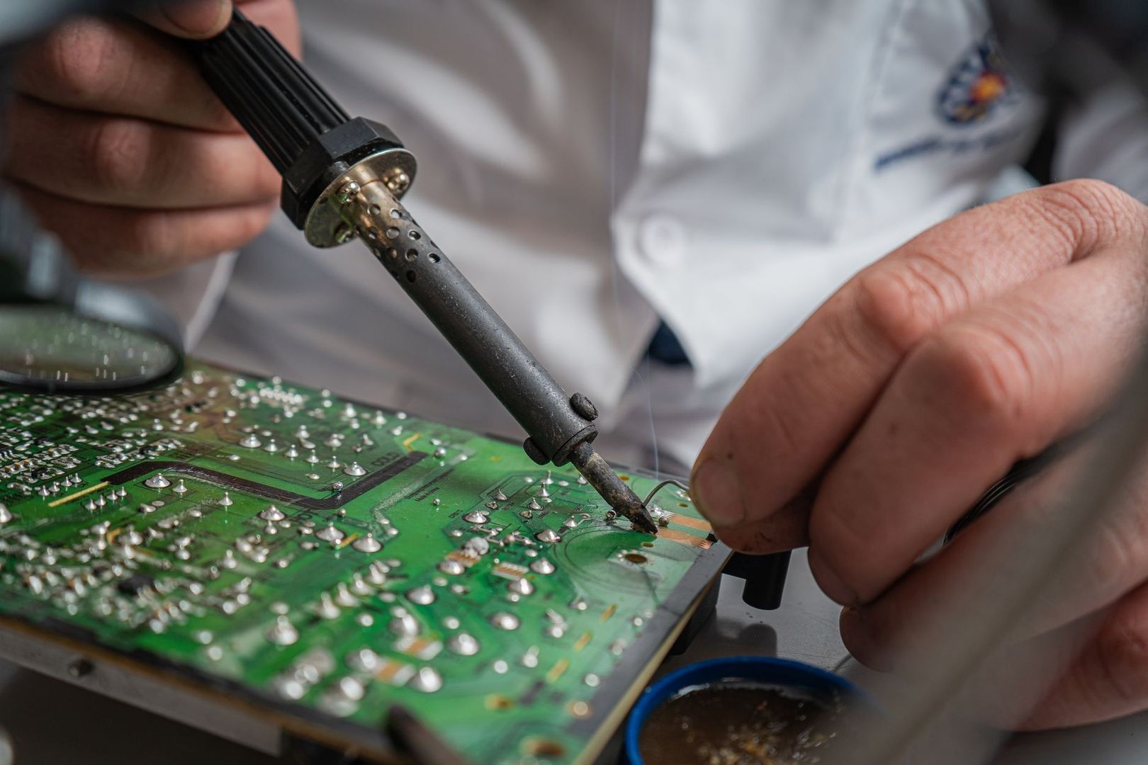 Hände reparieren eine Leiterplatte mit einem Lötkolben